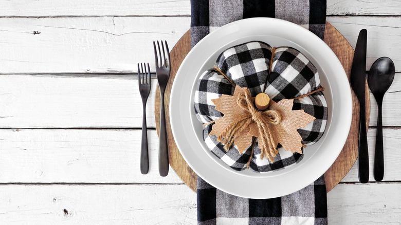 A fall table setting with buffalo plaid napkins and pumpkin flanked by silverware