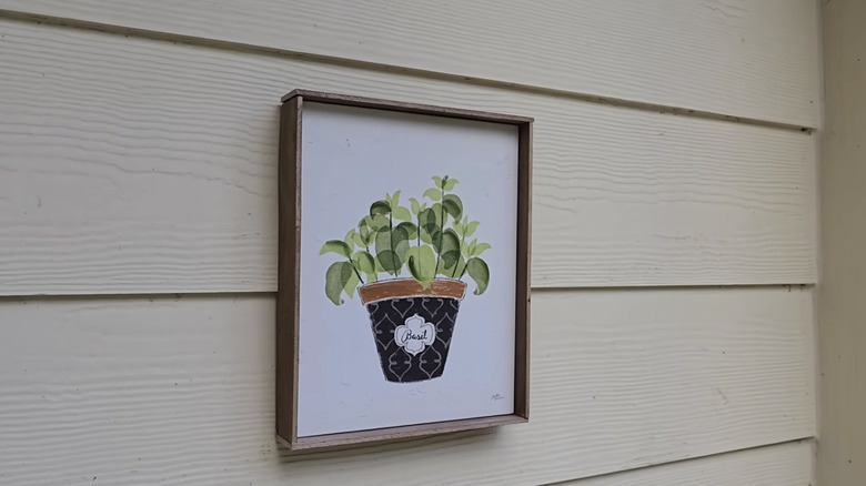 Illustration of a basil plant surrounded by a paint stir stick frame hanging on the exterior siding of a home