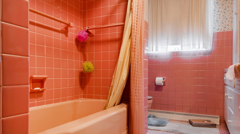 A 70s-style bathroom with small orange tiles, matching curtains, and white fixtures