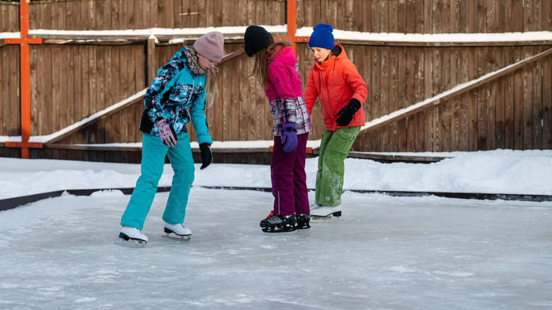 Three children ice skating on rink in yard