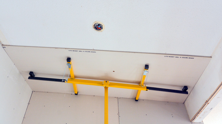 Drywall lift holding drywall sheet in place on ceiling