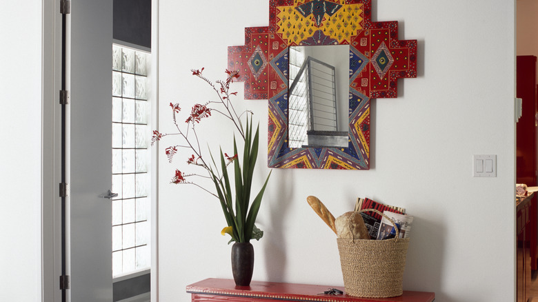 Entryway with bright tile mirror and red console table against a white wall