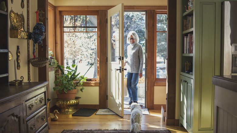 Woman stands in the doorway of an entryway, a dog stands to greet her