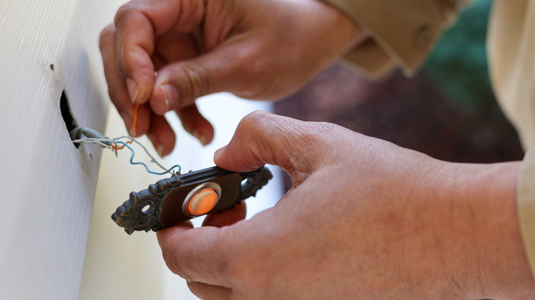 Person's hands holding wires on an old doorbell