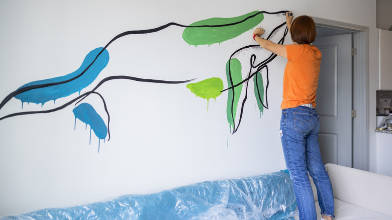 Person standing on couch, hand-painting wall