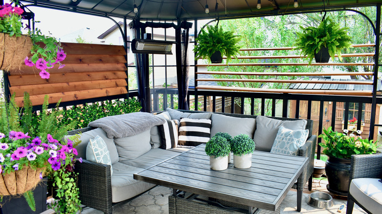 Covered patio with grey and black sofa and many plants and greenery