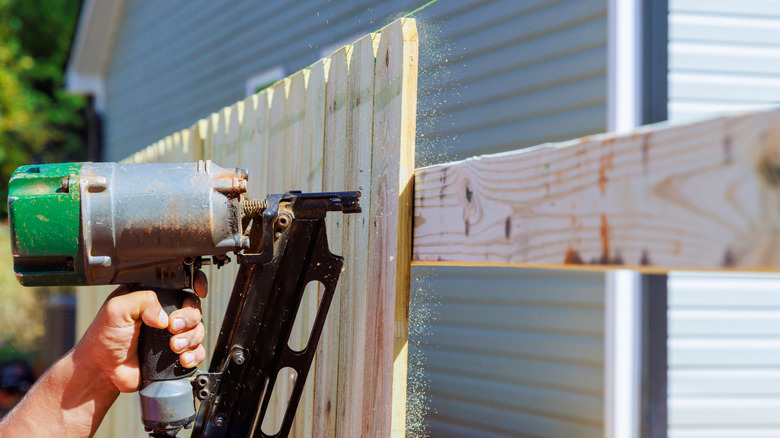 Person nailing pickets to the rails of a privacy fence