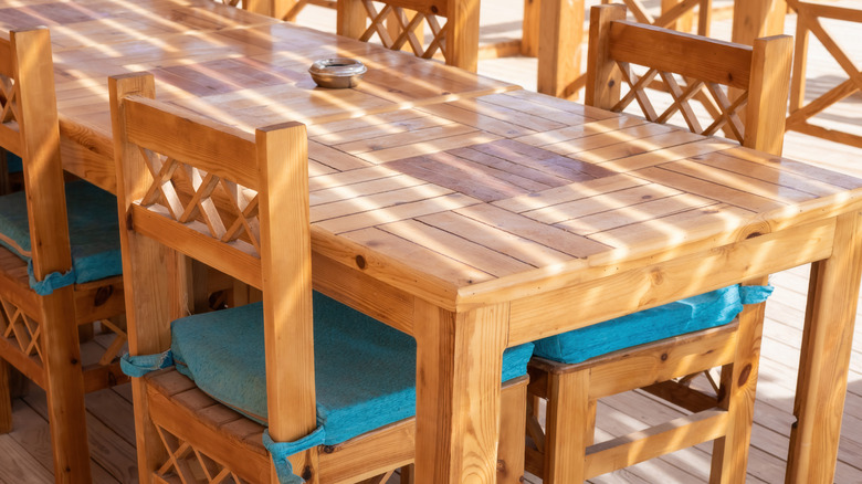 A sunlit wooden dining table with matching chairs set on a patio