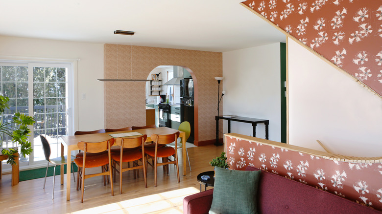 A modern open-plan living space with design touches reminiscent of the '60s, including Scandi-style dining furniture and bright, patterned wallpaper