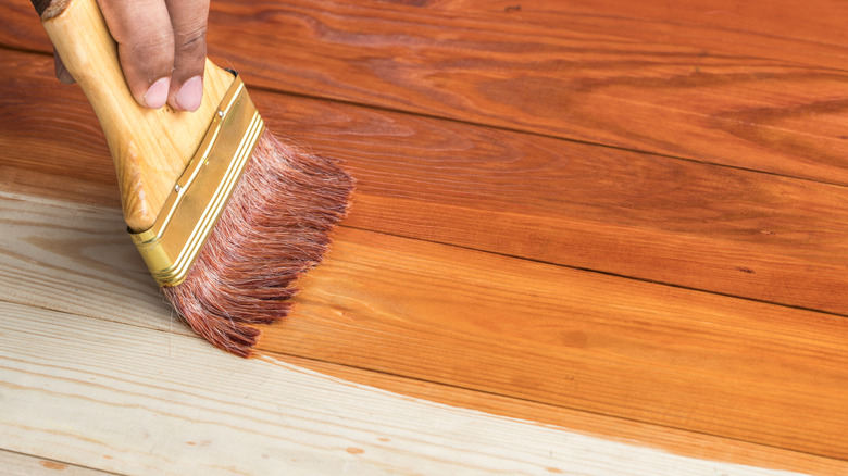 Person staining wooden furniture with a warm, walnut color