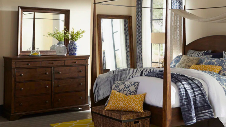 A canopy bed in a room with a wooden dresser.