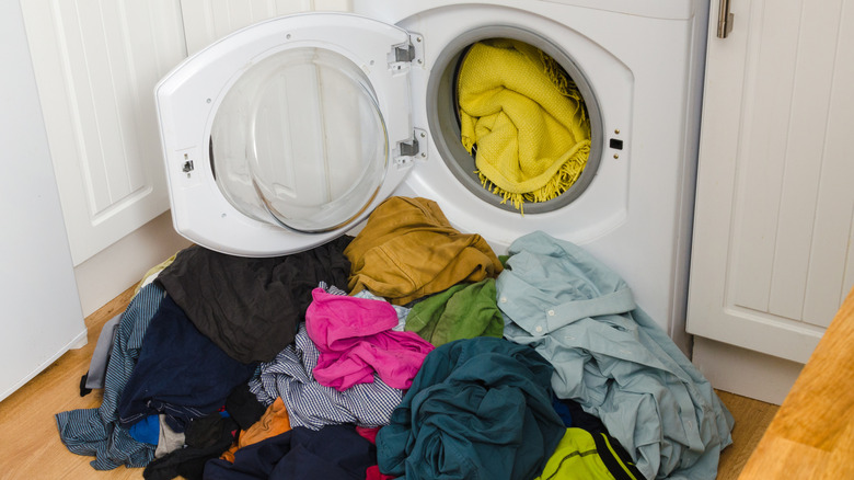 washing machine full of blankets with clothing piled on floor