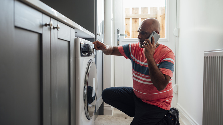 Man holding cell phone to ear, pressing washing machine touch screen