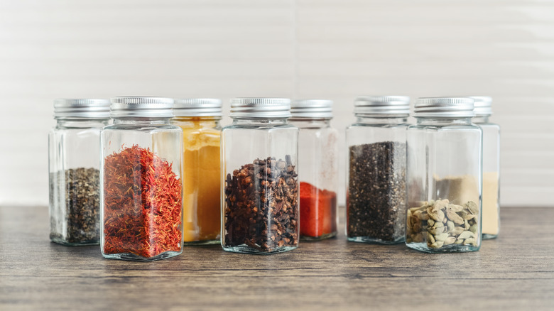 assorted spices in glass jars with metal lids on a kitchen table