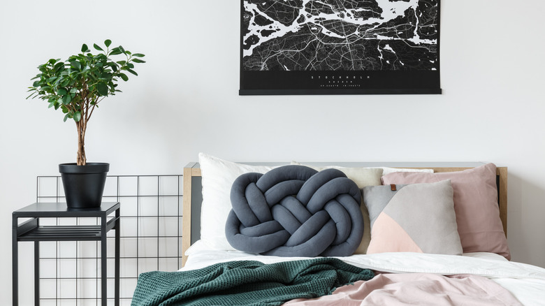 Blue knot pillow on a bed next to end table holding potted tree