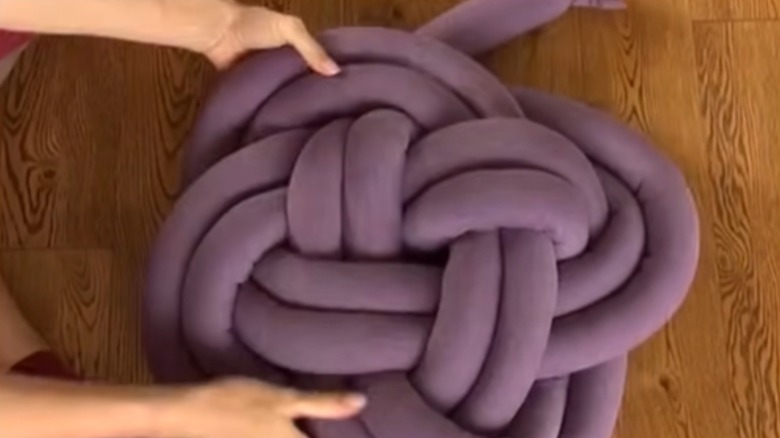 A pair of hands tie a fabric tube into an intricate knot pillow.