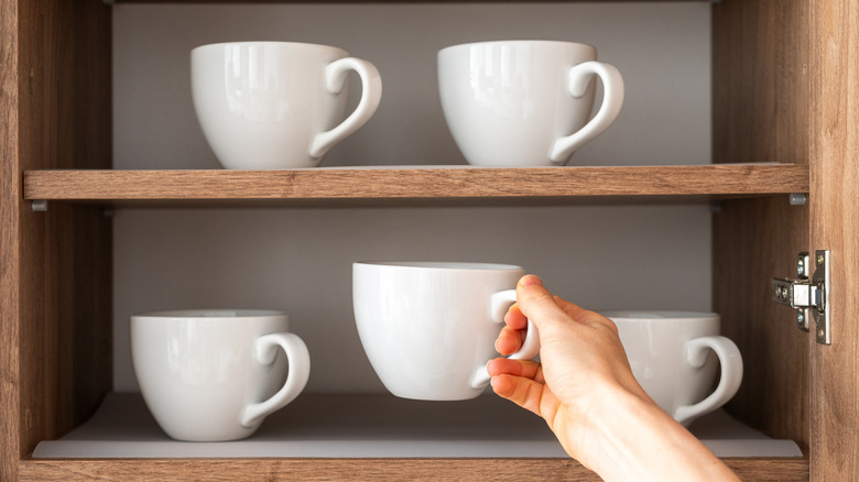 A woman grabbing a white mug from a cabinet
