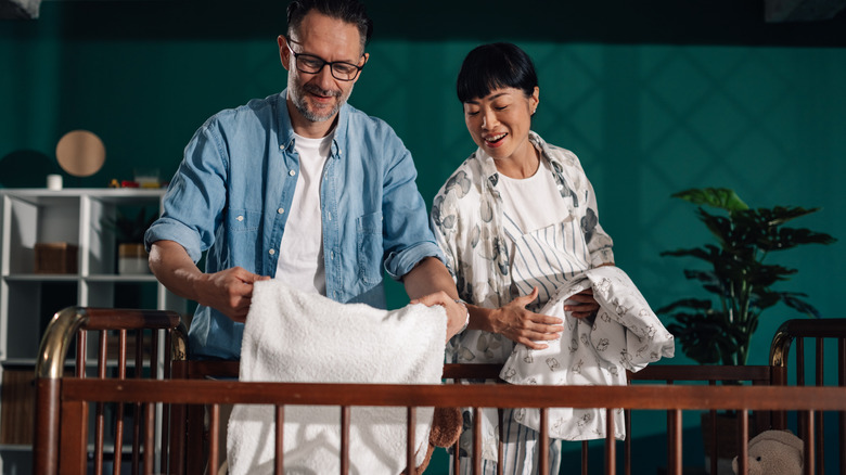 Two parents prepare bedding for their baby's crib.
