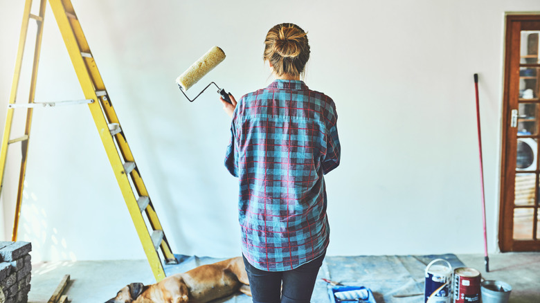 A woman with painting supplies faces a blank white wall
