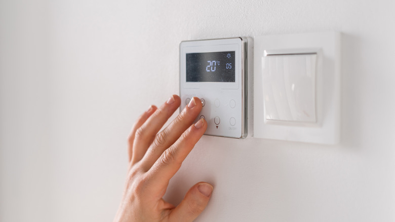 hand adjusting a thermostat on a wall next to a switch
