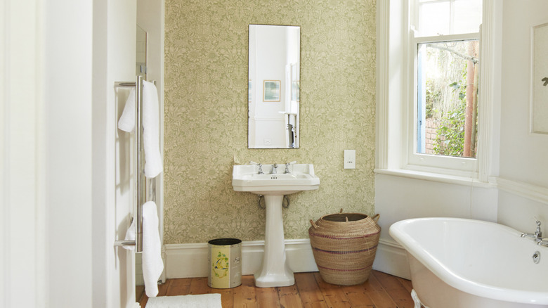 A light, lovely bathroom with a trash can and a hamper under a pedestal sink.