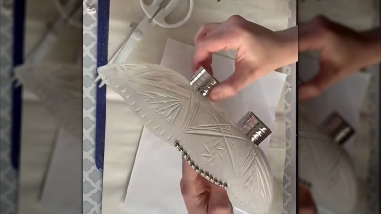 A person attaches metal napkin rings to the bottom of a painted Dollar Tree plastic bowl with glue.