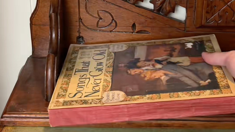 An old decorative wooden wall shelf upturned on a tabletop and used to store books.