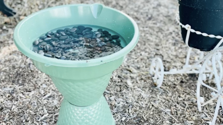 A light green birdbath made with an oil pan basin sitting atop two planters.