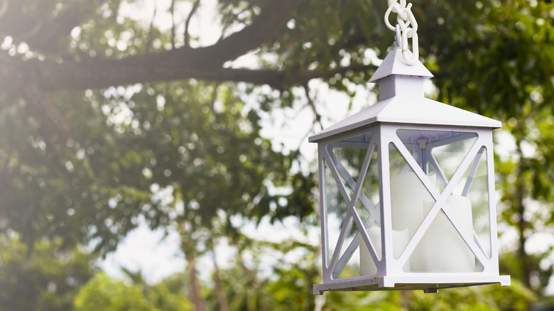 A lantern hanging outdoors holding three white candles