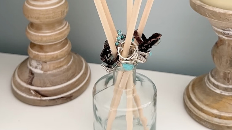 Rings hanging from wood dowels placed inside a clear glass bottle.