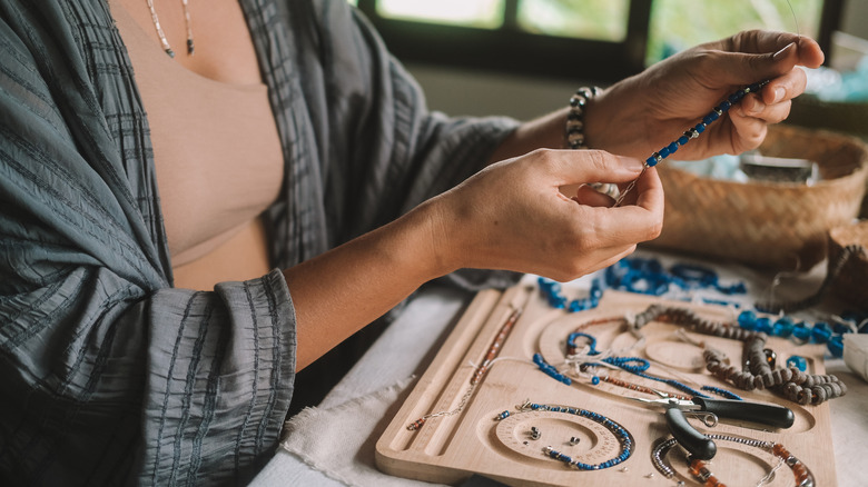 A woman holds up a piece of jewelry over her collection spread out on a table.