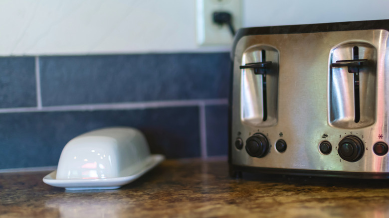 A plain white butter dish on a counter next to a toaster
