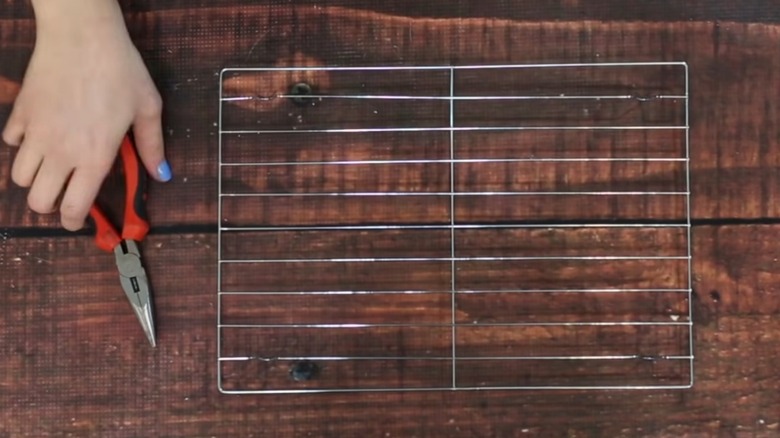 A hand holding a pair of pliers next to a Dollar Tree baking rack on a table.