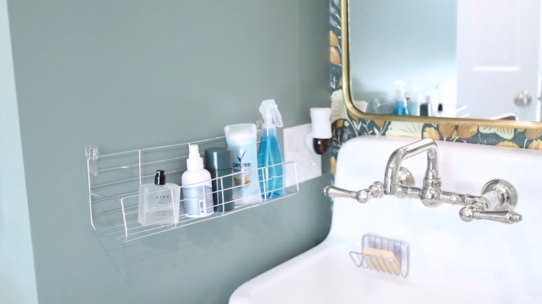 Soap, deodorant, and fragrances in a wire rack attached to a bathroom wall beside a sink.