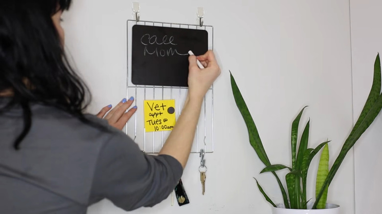Wire cooling rack hanging on wall with keys and blackboard.
