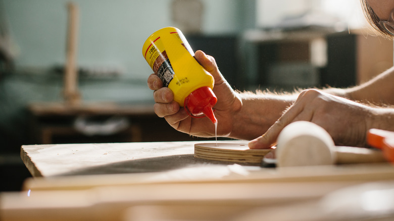 A man applying glue from a yellow bottle to a piece of wood
