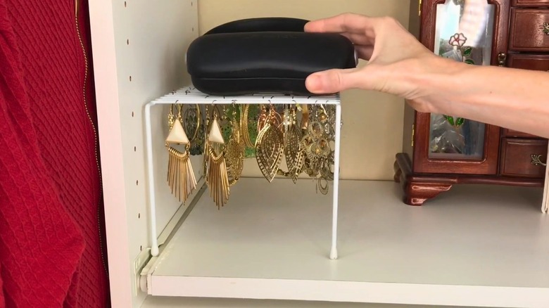 Woman places sunglasses case over white cabinet shelf