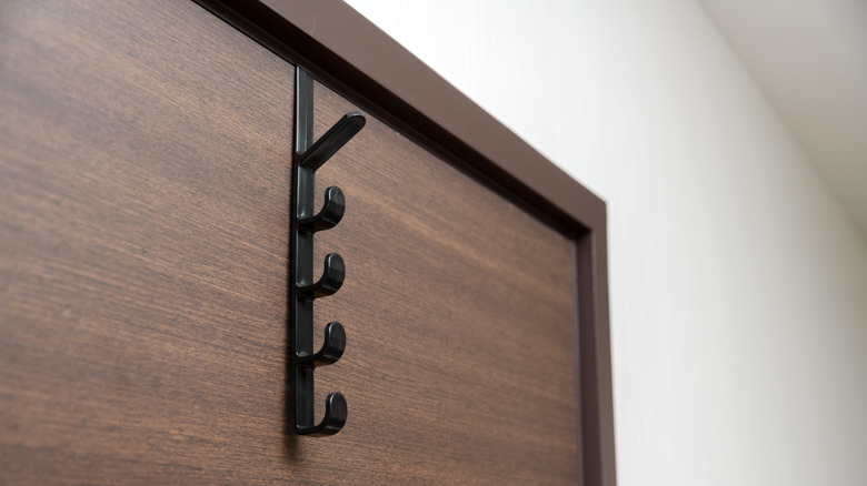 A black metal over-the-door hook hanging on a brown wooden door in a room with white-painted walls.
