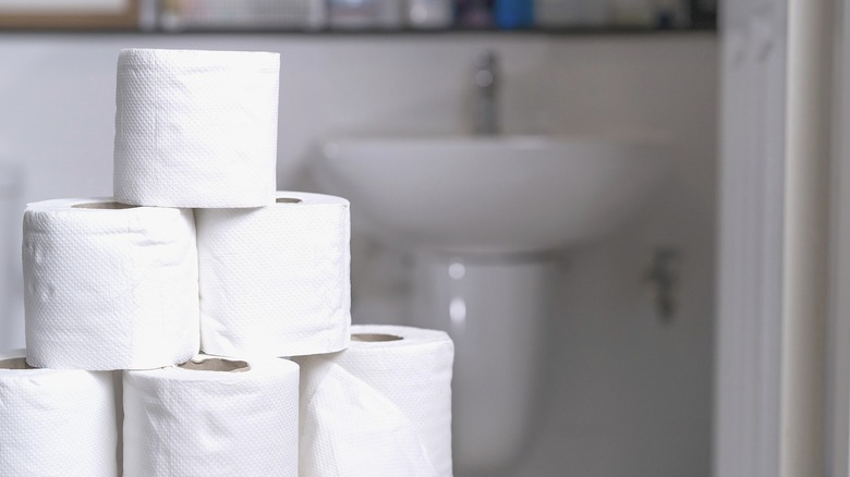 Rolls of toilet paper stacked up in the bathroom.