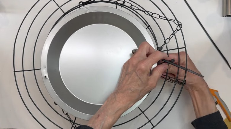 Photo showing hands tying the metal cake pan to the wreath and basket combo using zip ties