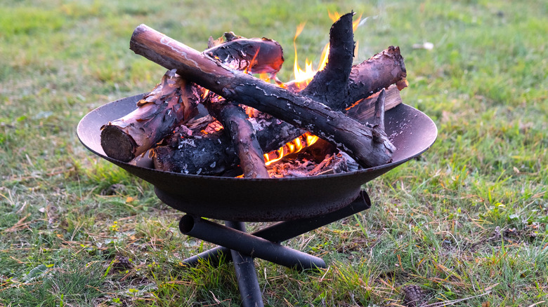 Portable fire pit filled with burning logs on a lawn