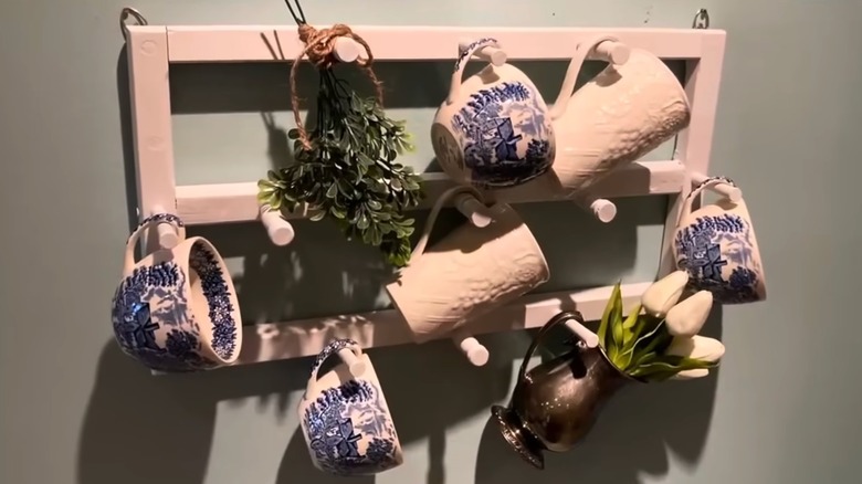Collection of coffee or tea mugs and plants hanging from a white mug storage rack that used to be a magazine rack