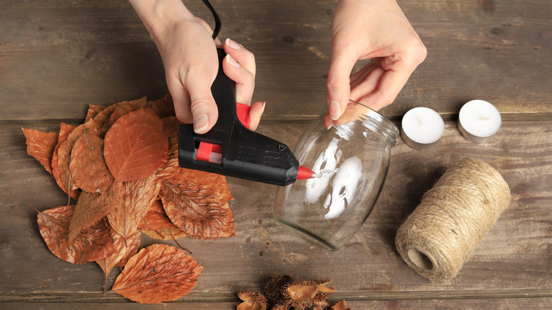 Woman adding hot glue to glass jar with leaves and twine