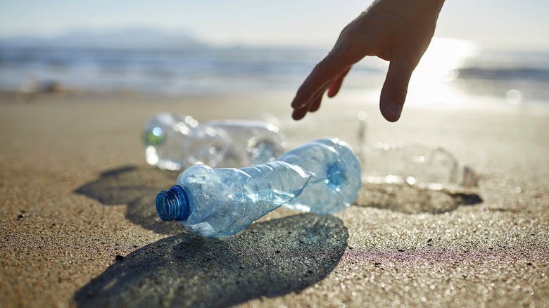 Close-up of person's hand reaching to grab plastic water bottles from beach