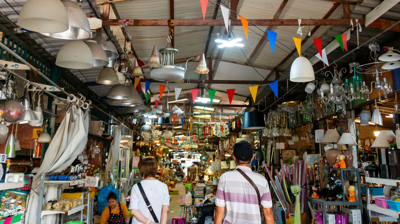 Two people walking down the aisle of a large, crowded thrift store full of retro home accessories.