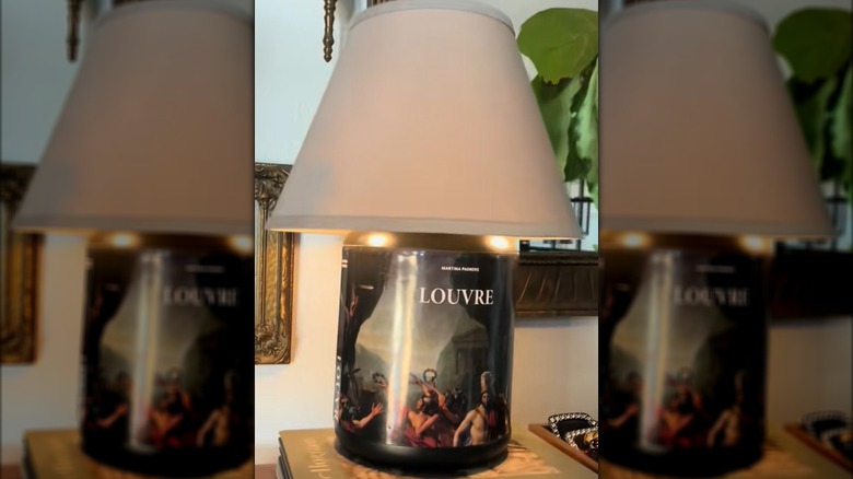 A black protein powder canister decorated with a Louvre book dust jacket is made into a lamp.