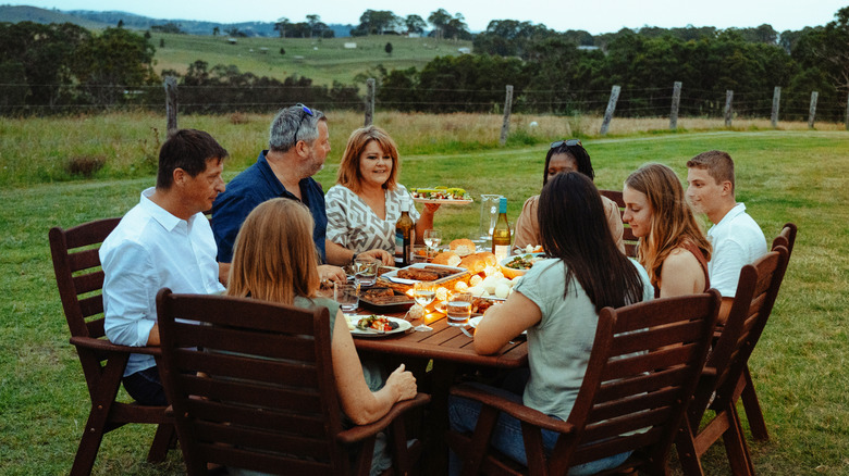 A family sitting outside, eating a meal at a table in the yard at dusk