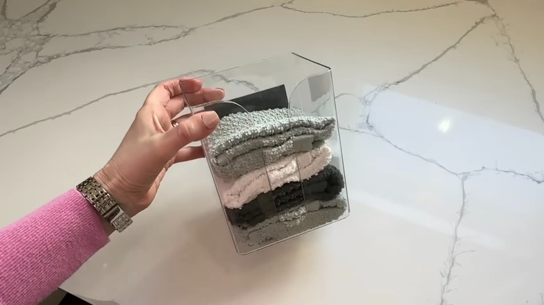 Woman holding a dollar tree dryer sheet holder filled with folded kitchen towels.