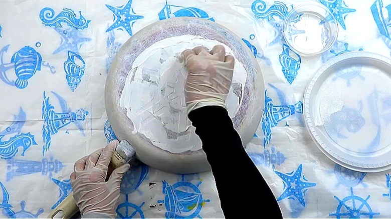A person wearing gloves applies paint to a frying pan with a sponge