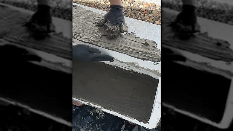Hands with black gloves smearing concrete mixture over a white Styrofoam cooler.